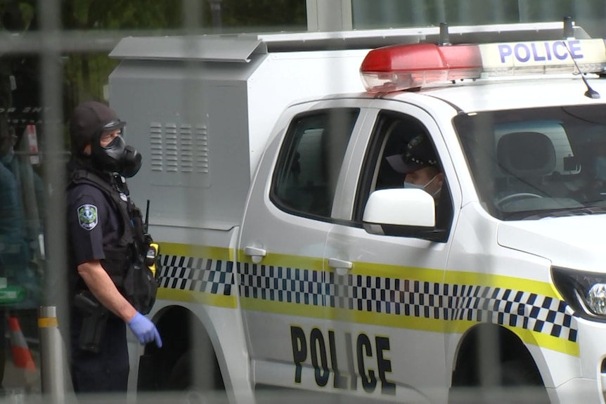 A police officer wearing a gas mask points at another police officer in the front seat of a wagon