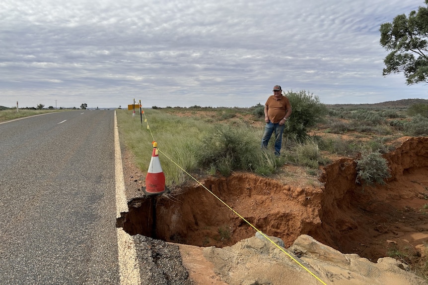 un hombre parado cerca de un gran agujero en una carretera del interior