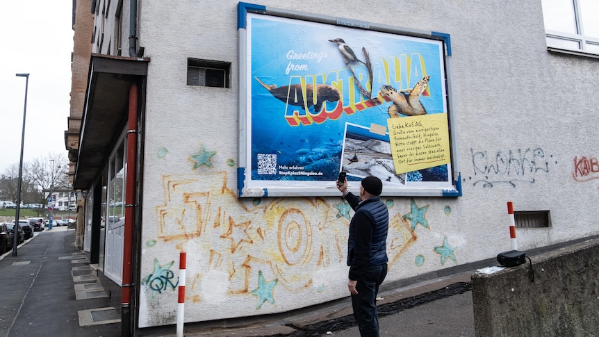 A bright postcard-style billboard on a brick wall features a sea turtle, bird, and dugong alongside a photo of a salt mound.