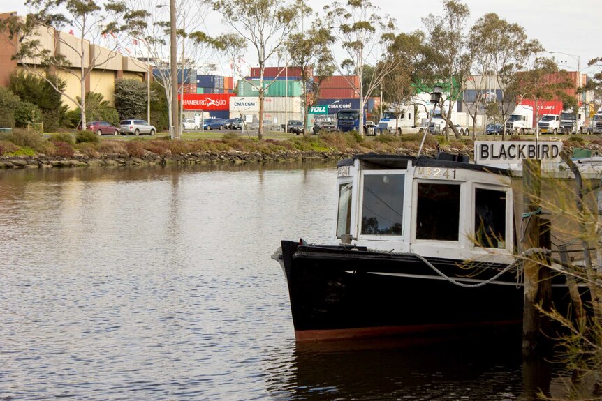 A small river boat, shipping containers in background.