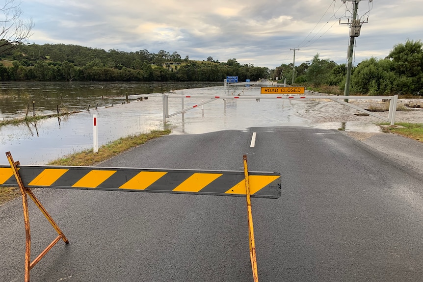 Floodwaters over a road, behind a road closed sign.