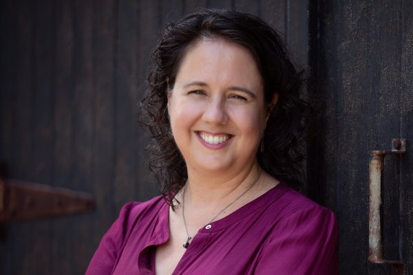 A woman with dark hair and a purple shirt smiles.