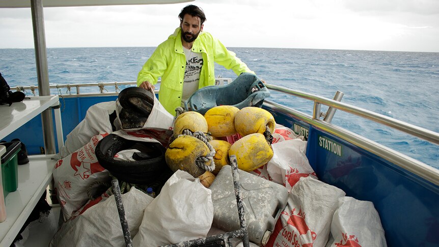 A volunteer stacks and sorts rubbish on the back deck of a boat.