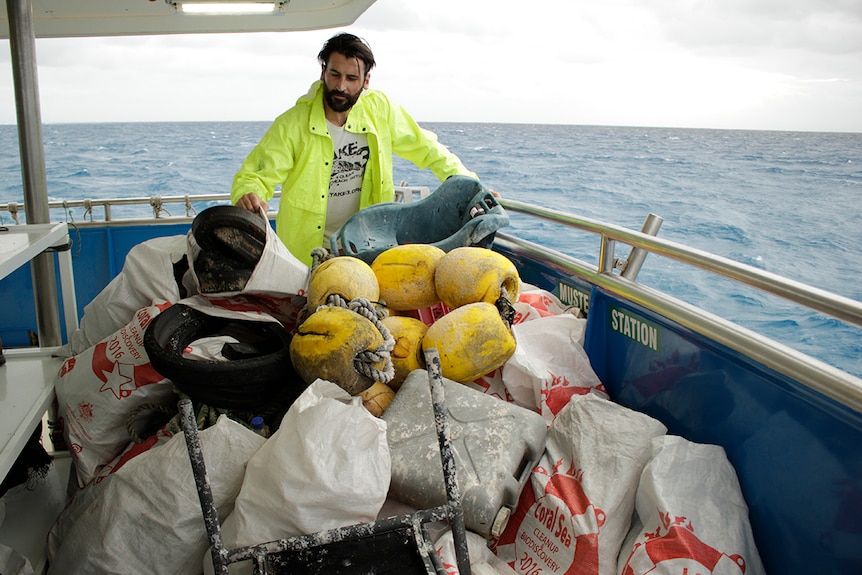 A volunteer stacks and sorts rubbish on the back deck of a boat.