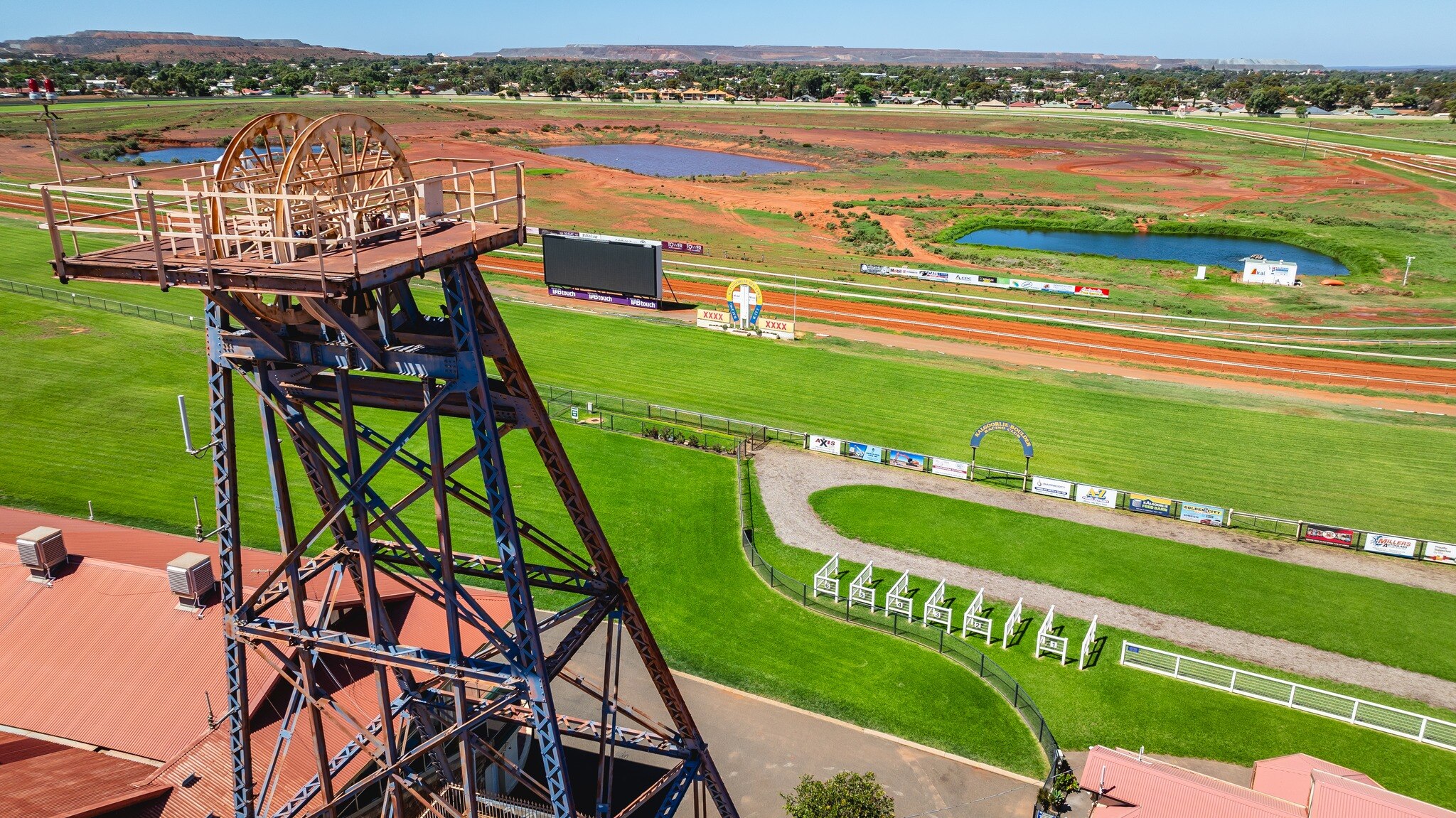 Una vista aérea del hipódromo de Kalgoorlie con césped verde y un cabezal minero en primer plano.  