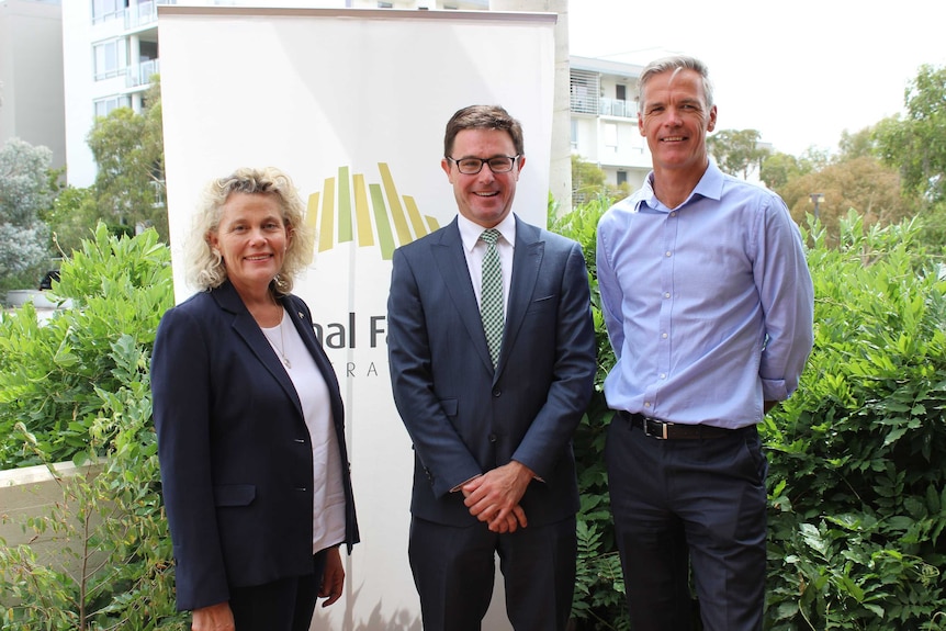 Three people smile for the camera in front of a National Farmers Federation sign