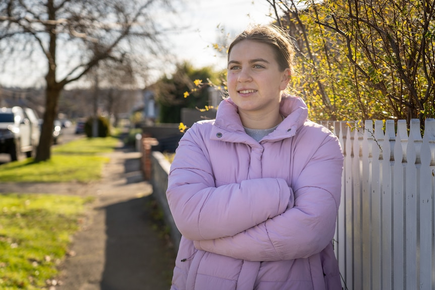 a young woman leans against a fence and looks into the distance.