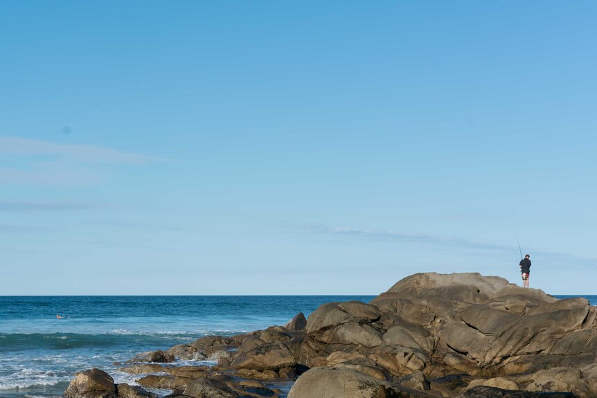 A man fishes from the rocks at Coolum Beach, June 10, 2016