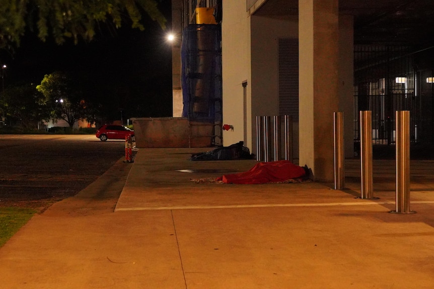 Two people sleeping on the ground outside a building at night