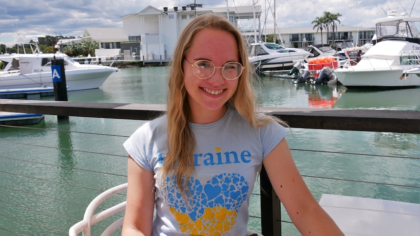 Young woman with blonde hair and glasses wears shirt with 'Ukraine' written on it and smiles at the camera
