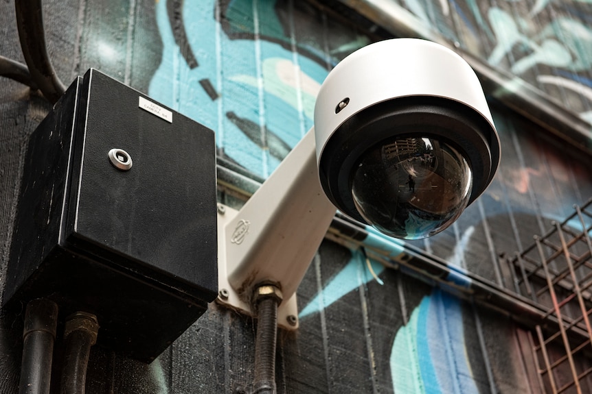 A dome CCTV camera installed on a wall with blue graffiti on it