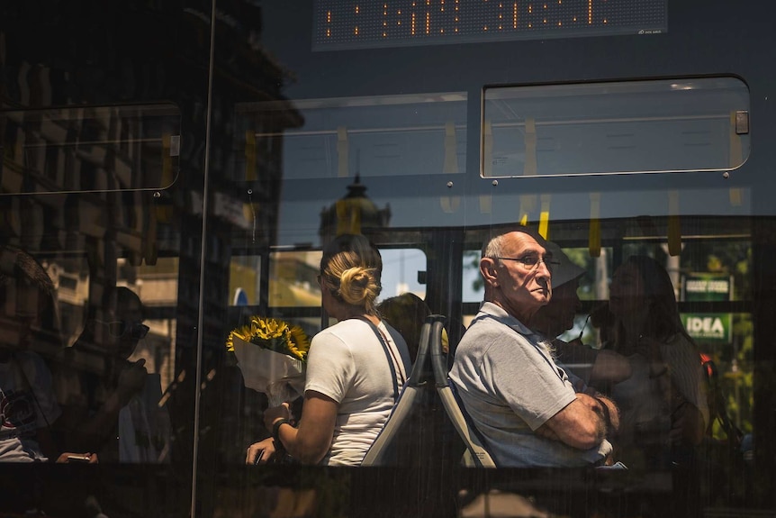 A young woman and an older man sit on a bus facing in opposite directions.