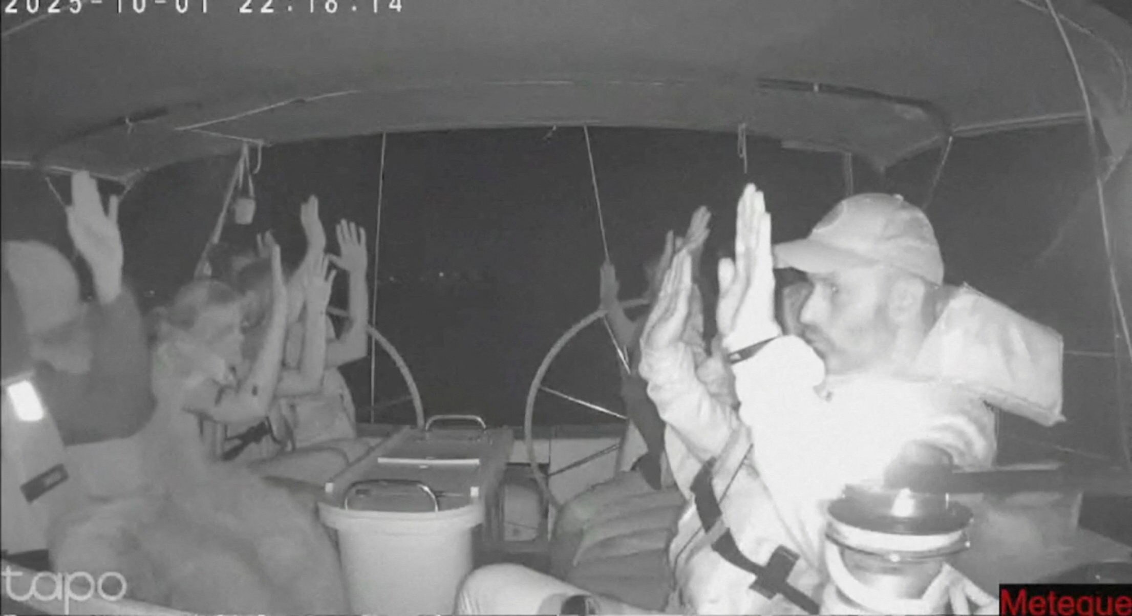 people on a boat sit with their hands raised in the air waiting to be boarded