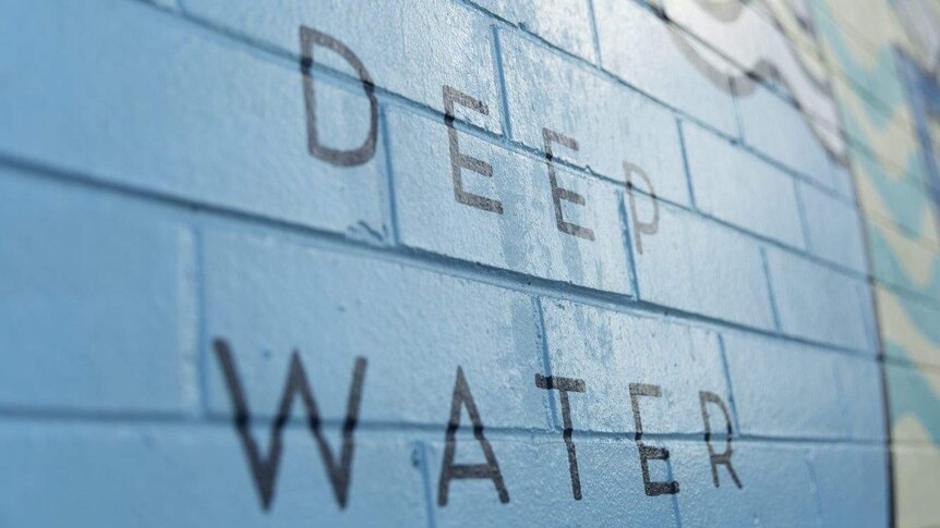 A painted blue brick wall at a pool signing 'deep water' in black letters.