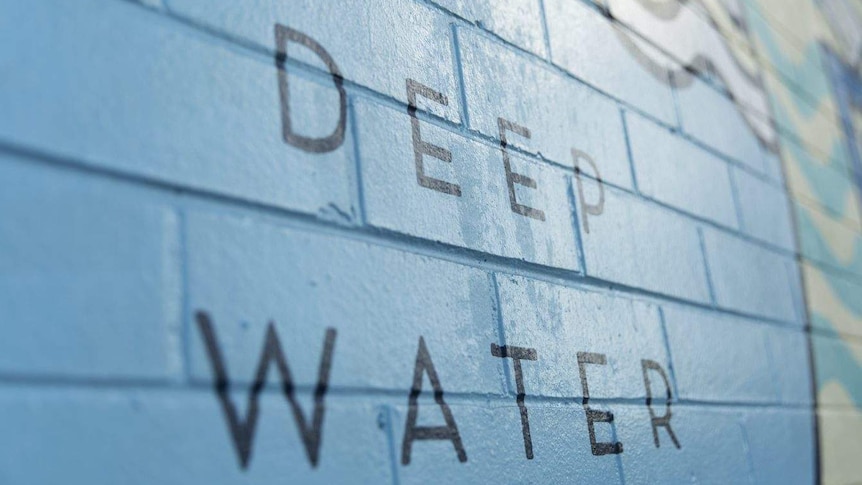 A painted blue brick wall at a pool signing 'deep water' in black letters.