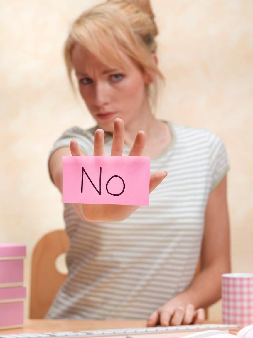 Woman at desk with arm outstretched with pink sticky note saying 'no' on on her palm