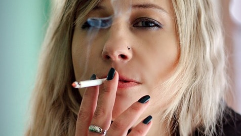 A young woman with blonde hair smokes a cigarette.
