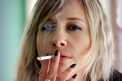 A young woman with blonde hair smokes a cigarette.
