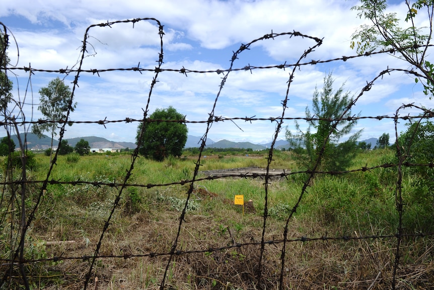 A barb wire fence in front of a field. 