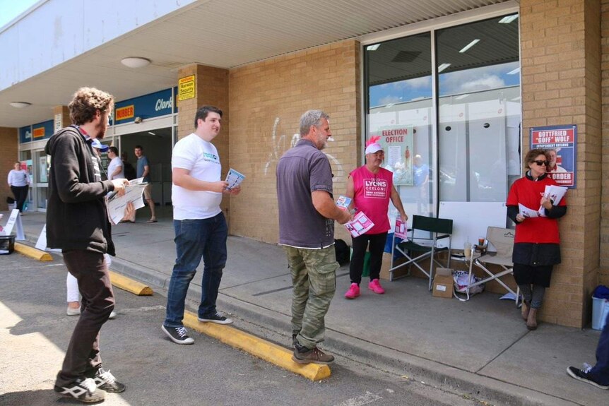 Campaign workers wait to hand out how-to-vote cards at an early voting centre.