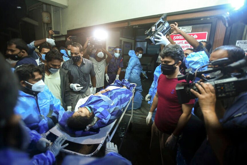 One of the persons injured on a stretcher, surrounded by media, directly after an India Express flight crashed.