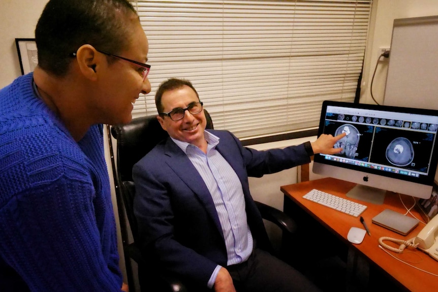 Dr Rogers points at a brain scan on a computer screen as Hare Haro looks on.