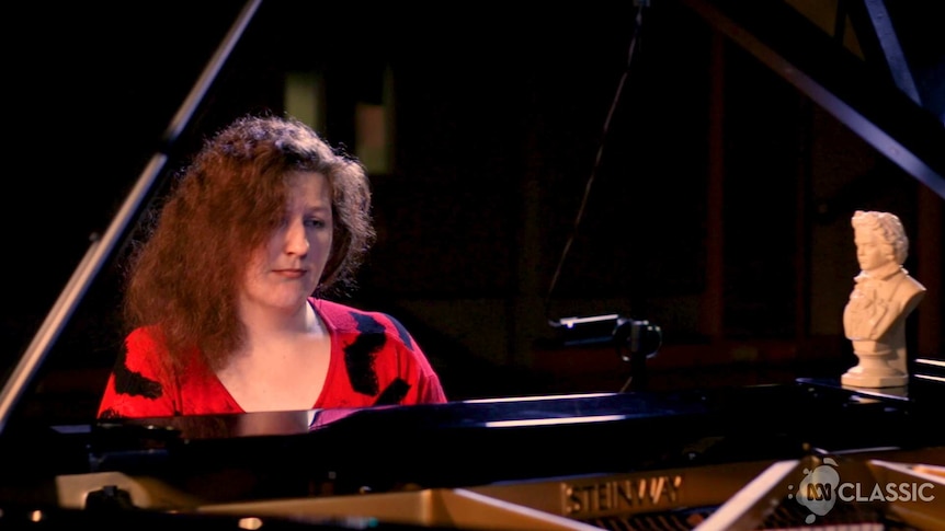 A woman with red hair sits at a piano