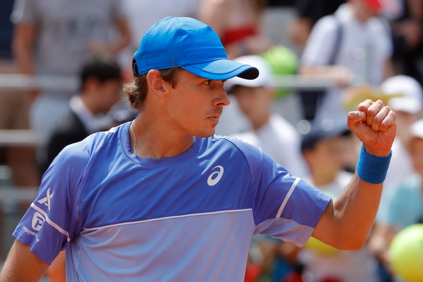 Tennis player Alex de Minaur, wearing a blue shirt and cap, clenches his fist during a tennis match.