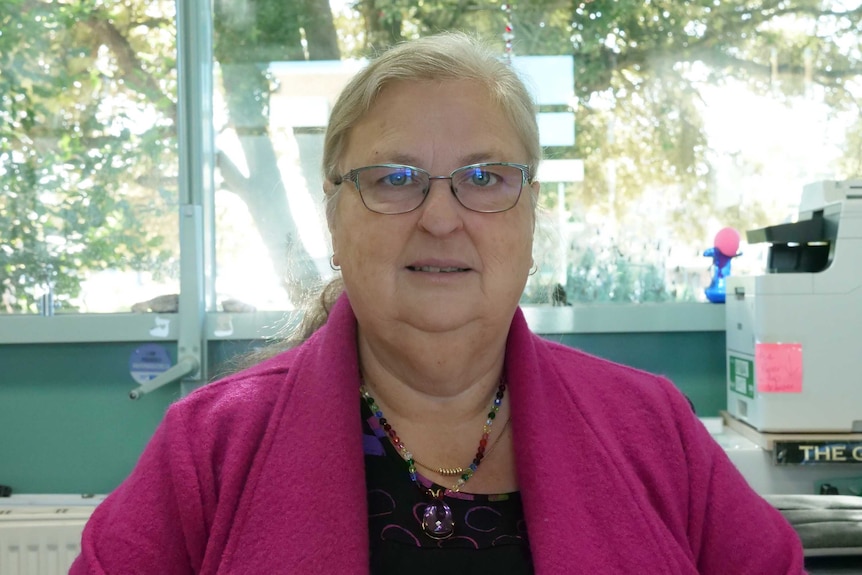 A woman wearing glasses sits in front of an office window