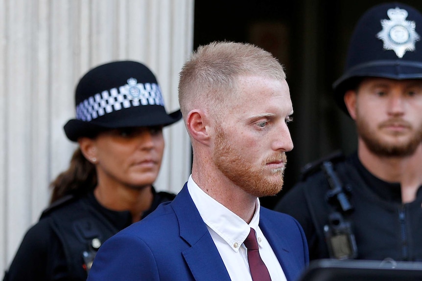 A red headed man leaves Bristol Crown Court with two police officers in the background.