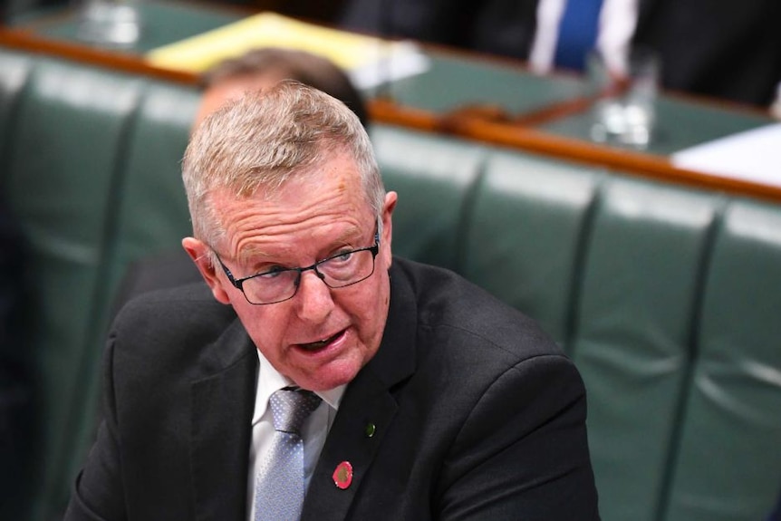 Man in suit and glasses speaking at Parliament House.