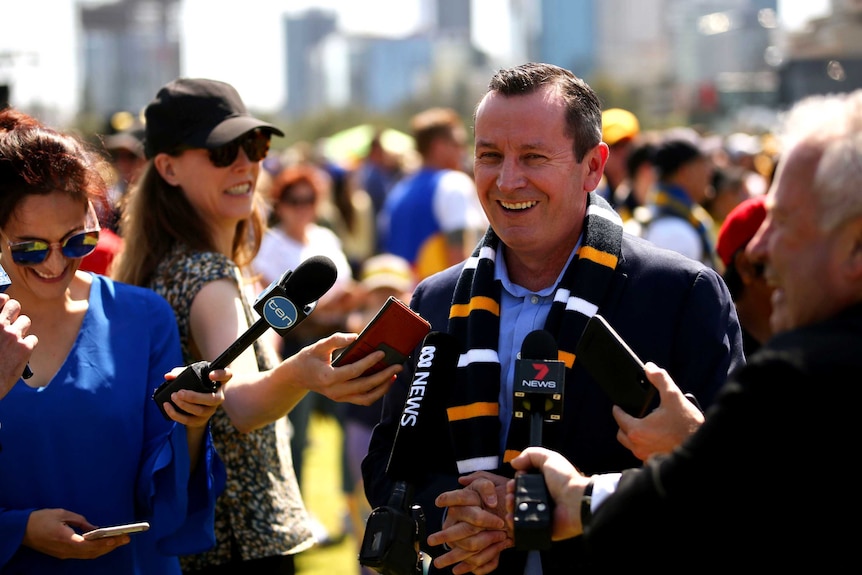 The premier wearing an Eagles scraf laughs with surrounding Perth media.