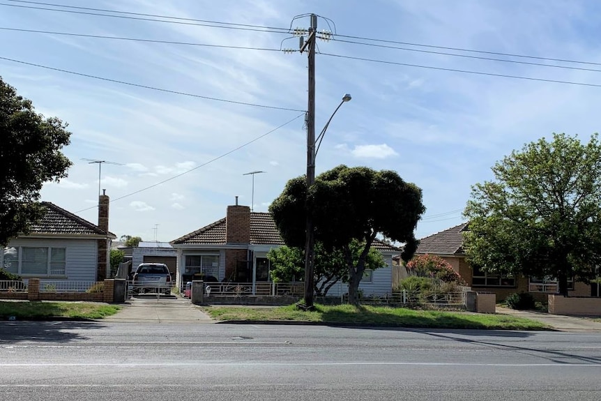 A white weatherboard house with brick chimney and tiled roof. A silver SUV sits in the driveway.