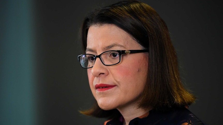 A close-up photograph of Jenny Mikakos, a woman with dark hair and glasses, speaking at a press conference.
