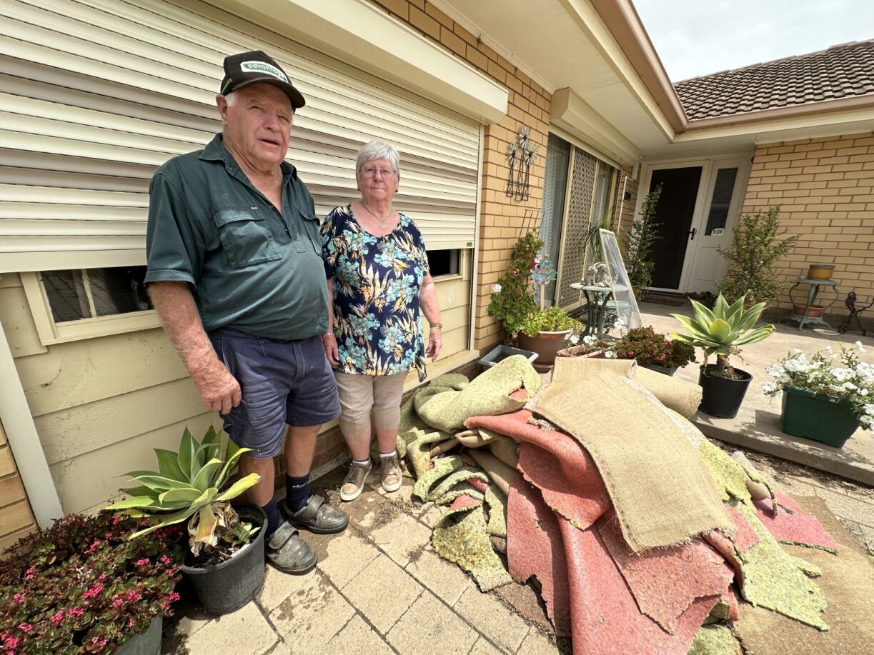A couple in the middle age standing in front of torn up carpet following floods.