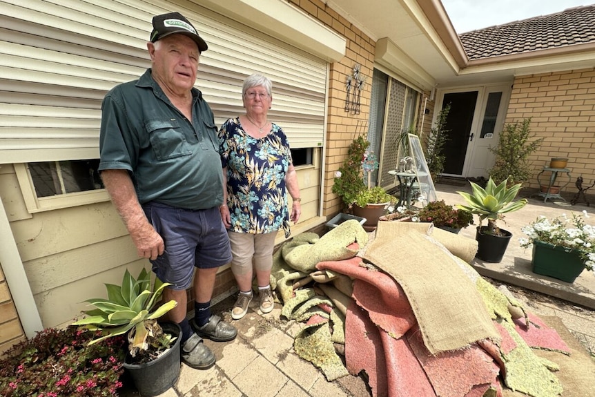 A couple in the middle age standing in front of torn up carpet following floods.