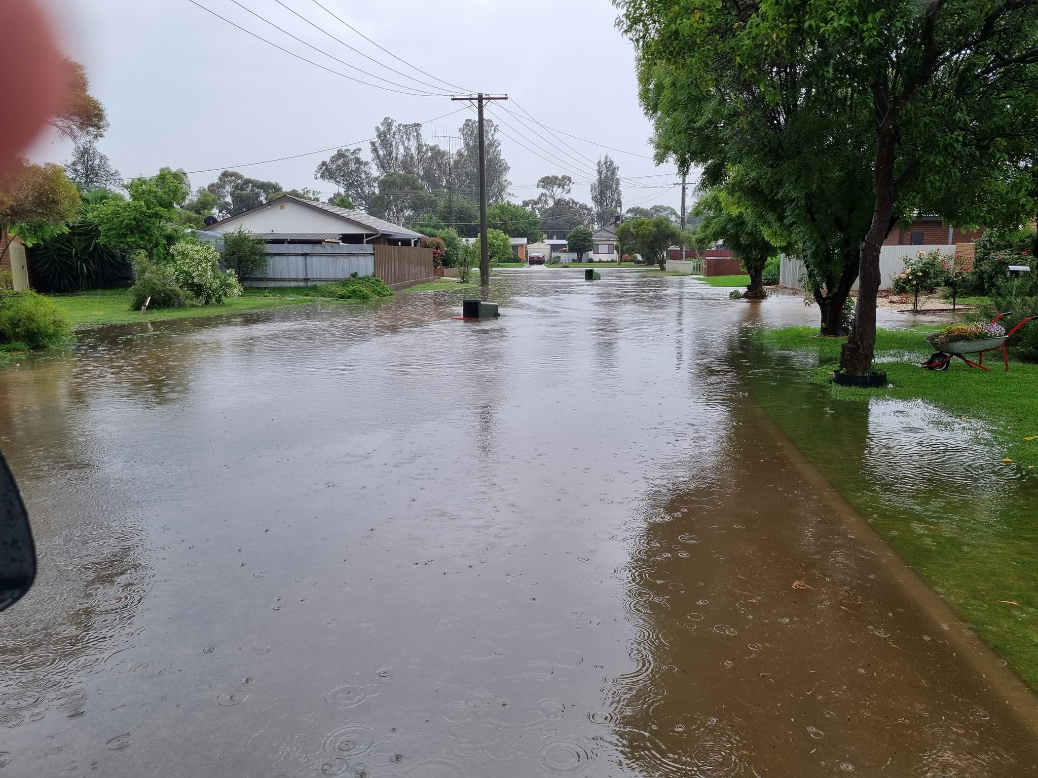 A residential court with a flooded road and gardens with houses and trees in the background
