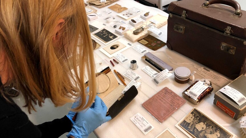 A Museums Victoria staff member inspects the contents of a WWI soldier's suitcase with a magnifying glass.