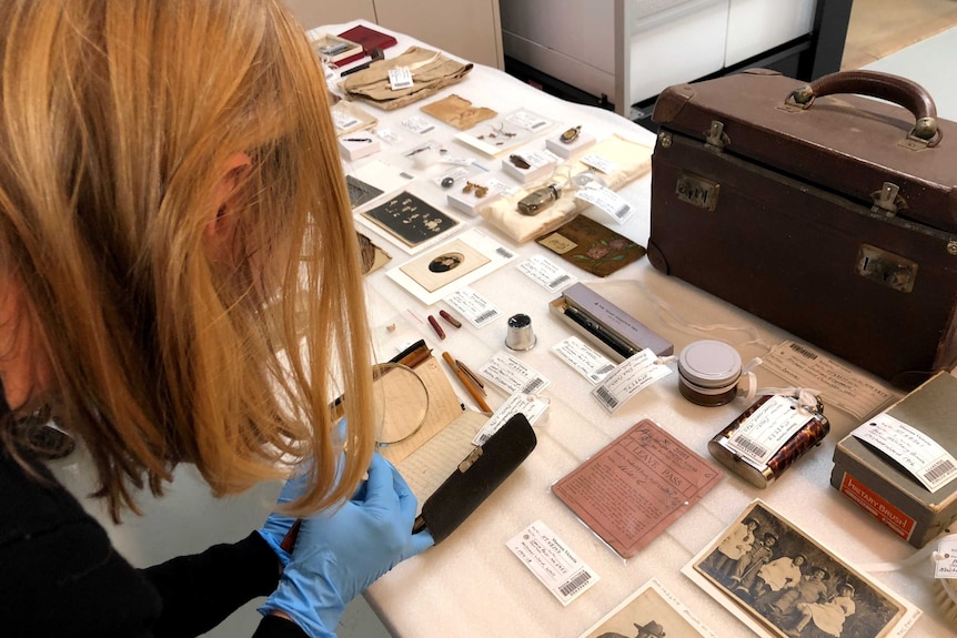 A Museums Victoria staff member inspects the contents of a WWI soldier's suitcase with a magnifying glass.