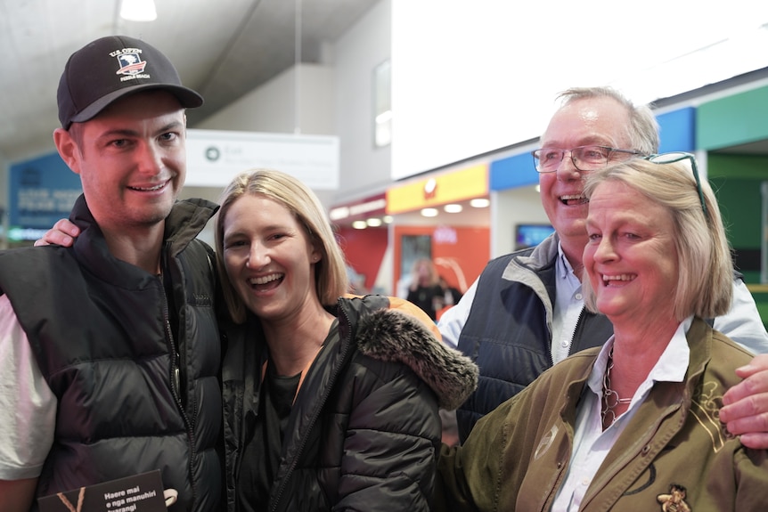 An embracing young couple meet a smiling elderly couple.