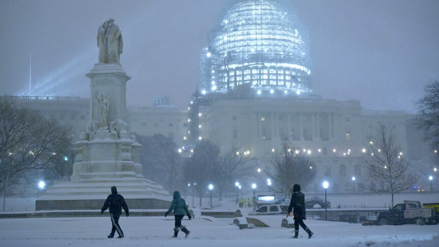 Pedestrians in front of the snowy US Capitol in Washington DC, as snow continues to fall.