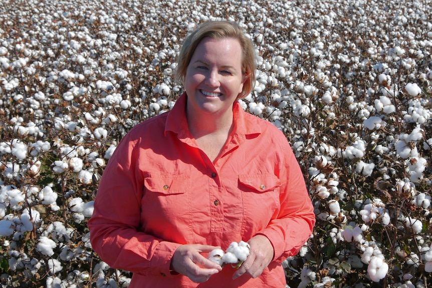 A woman with blonde hair wearing a cotton red button up shirt in a field of cotton
