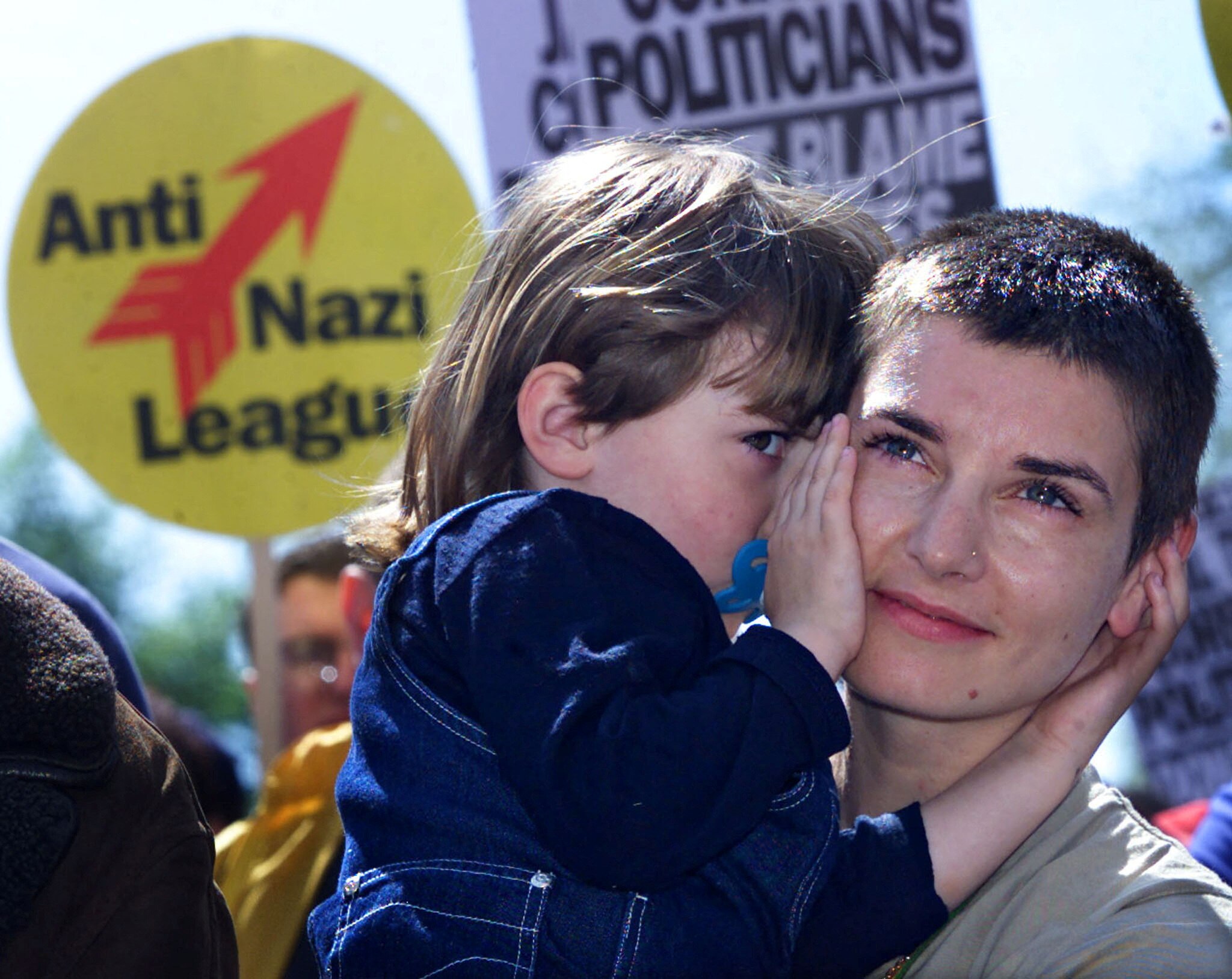 Women with shaved head holds little girl with signs of protest behind her 