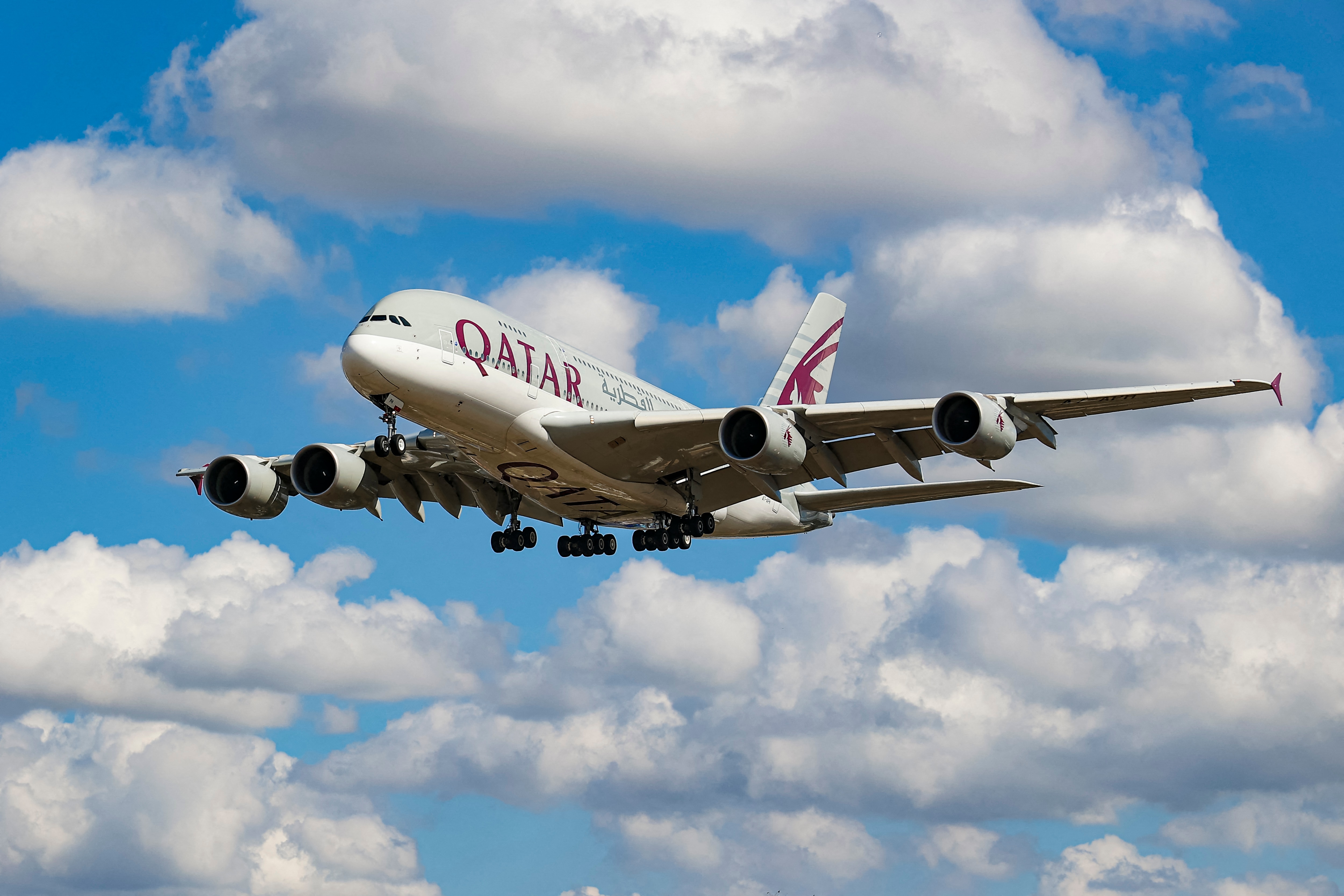 A Qatar Airways Airbus plane flying in a blue sky full of white clouds.