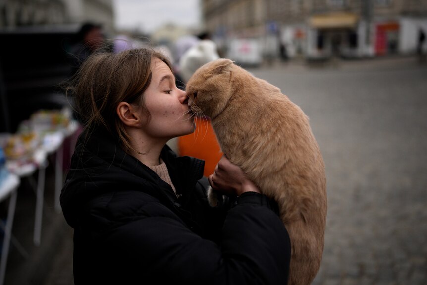 A young woman holds her face up to the face of a ginger cat she is holding