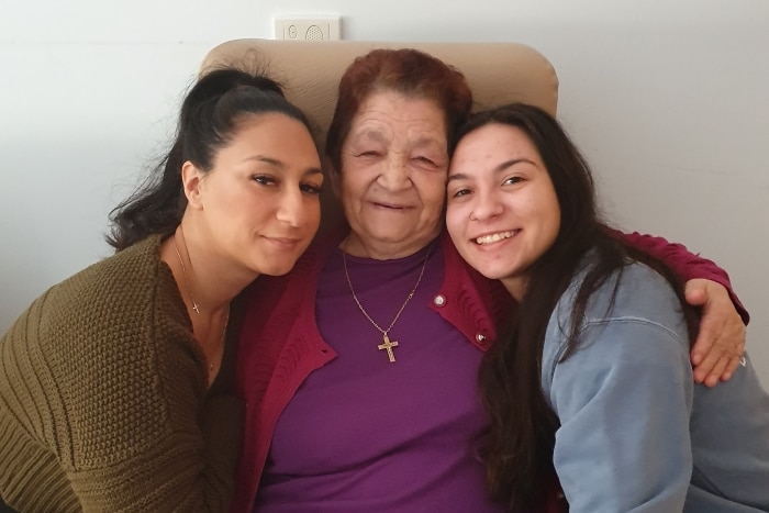 Maria Vasilakis hugs her granddaughters Silvana and Mary as she sits in a chair.