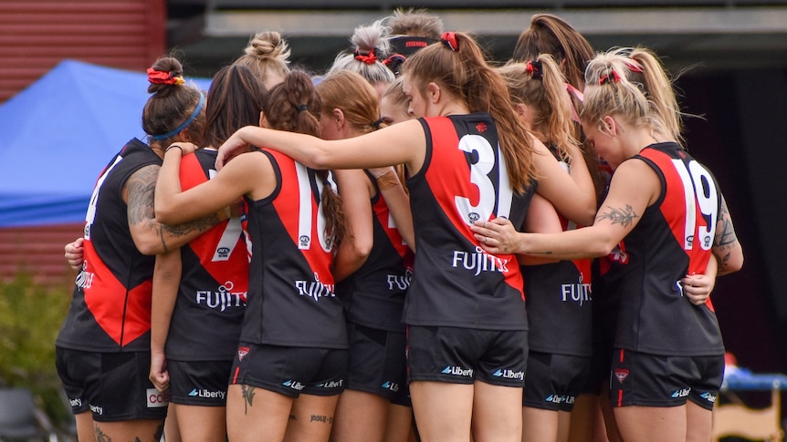 Essendon's VFLW team group in a huddle during a match in 2021.