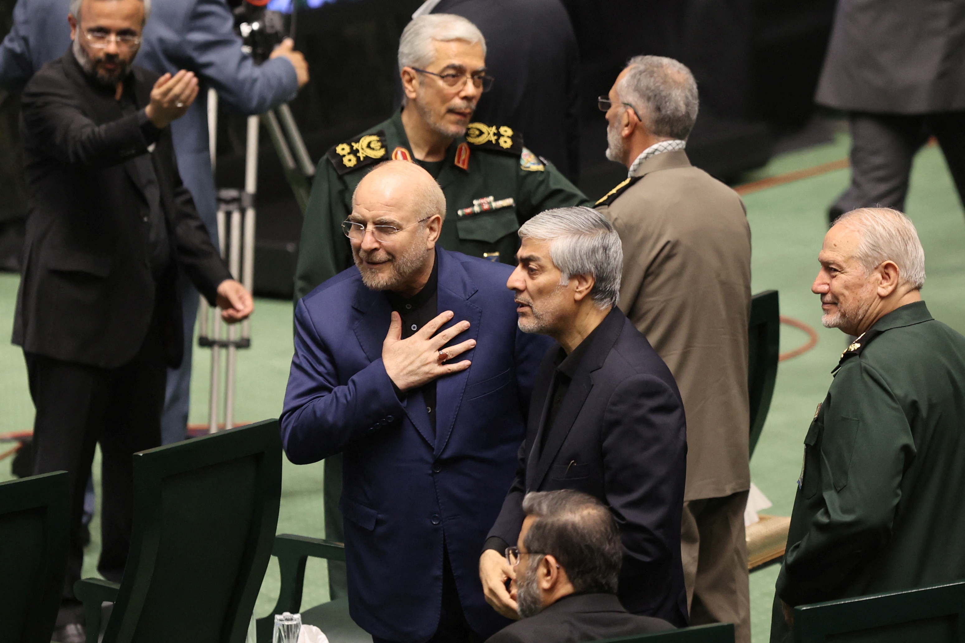 Mohammad Bagher Ghalibaf holds a hand to his chest as he walks in a suit through Iran's parliament.