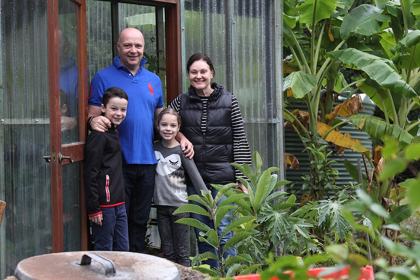 A man and woman standing with their two children in the doorway of a greenhouse, with banana trees in the background.