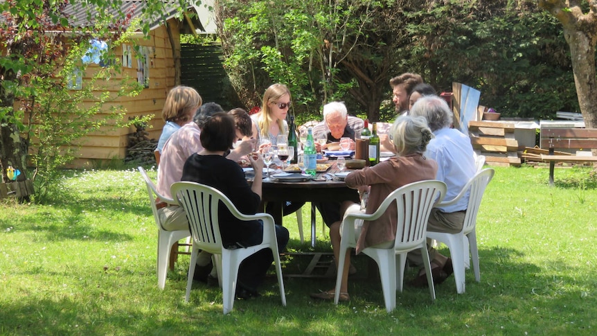 David Goodall sits slumped at the head of a table outdoors, his family filling the seats, sharing lunch in the sunshine